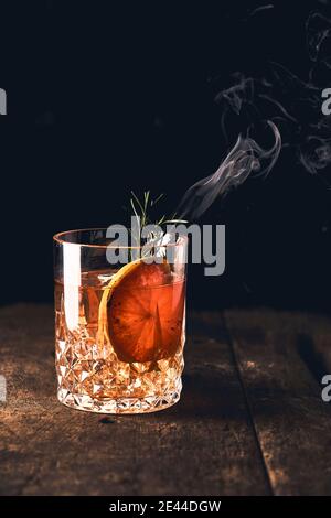 Glänzendes Glas frischer Negroni Cocktail mit Orangenscheibe garniert Mit brennendem Rosmarinzweig Stockfoto