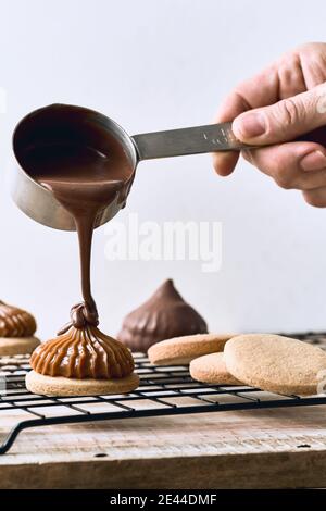Crop anonyme kochen Gießen Schokolade Sahne auf Cookies mit Karamell Auf weißem Hintergrund auf dem Tisch platziert Stockfoto