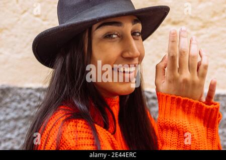 Modische junge ethnische Brünette in leuchtend orange Strickmode und schwarz hut und Blick auf die Kamera Stockfoto