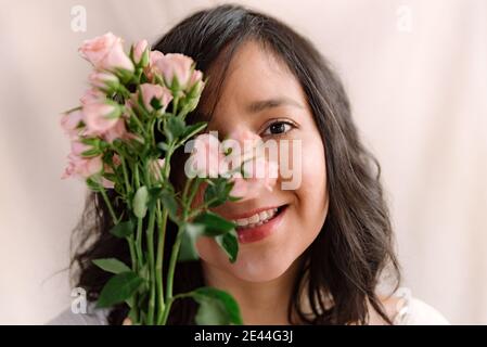 Porträt einer lächelnden jungen Frau mit rosa Rosen und natürlichen Look. Nahaufnahme im Frühling. Fröhlicher und glücklicher Ausdruck mit weit geöffneten Augen. Konzept Stockfoto