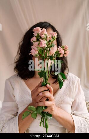 Porträt einer lächelnden jungen Frau mit rosa Rosen und natürlichen Look. Nahaufnahme im Frühling. Ernster Ausdruck mit weit geöffneten Augen. Konzept der glücklich Stockfoto