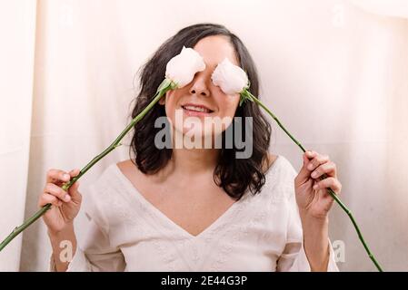 Lustiges Porträt einer lächelnden jungen Frau mit rosa Rosen auf ihrem Gesicht und natürlichen Look. Nahaufnahme im Frühling. Fröhlicher und glücklicher Ausdruck mit Augen Stockfoto