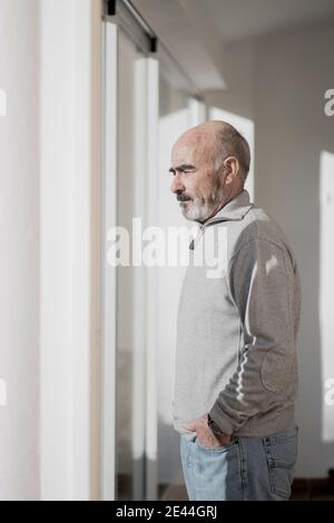 Entspannender älterer Mann zu Hause mit Blick aus dem Fenster Ein sonniger Wintertag Stockfoto