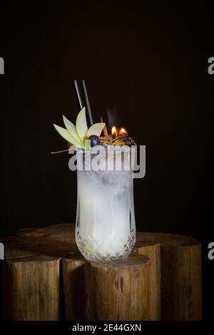 Ein Glas frischer Cocktail garniert mit Apfelscheiben und Brennen Gewürze auf Holztisch in schwarzem Hintergrund Stockfoto