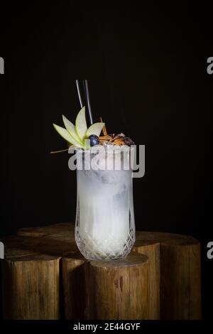 Ein Glas frischer Cocktail garniert mit Apfelscheiben und Brennen Gewürze auf Holztisch in schwarzem Hintergrund Stockfoto