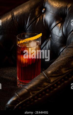 Glänzendes Glas frischer Negroni Cocktail mit Orangenscheibe garniert Mit Orangenschale auf Ledersessel Stockfoto