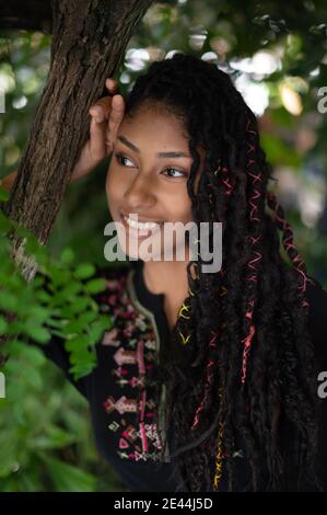 Porträt einer attraktiven afro latina Frau mit Dreadlocks, die neben einem Baum stehen Stockfoto