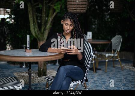 Junge attraktive afro latina Frau mit einem Smartphone in einem Restaurant Stockfoto