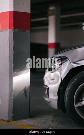 Modernes Auto mit gebrochenem Scheinwerfer und beschädigte Stoßstange in der Nähe geparkt Betonsäule nach Unfall in der Garage Stockfoto