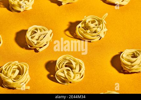 Von oben Set von rohen fettuccine Pasta Nester auf gelegt Hellgelber Tisch Stockfoto