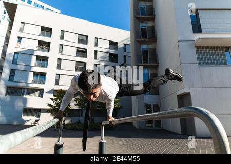 Männlicher Unternehmer in edlem Anzug Balancing in Handstand auf Metall Geländer in der Stadt, während vorformende Parkour Trick Stockfoto