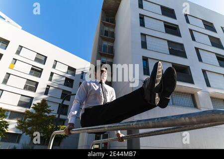 Männlicher Unternehmer in edlem Anzug Balancing in Handstand auf Metall Geländer in der Stadt, während vorformende Parkour Trick Stockfoto