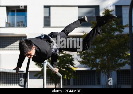 Männlicher Unternehmer in edlem Anzug Balancing in Handstand auf Metall Geländer in der Stadt, während vorformende Parkour Trick Stockfoto