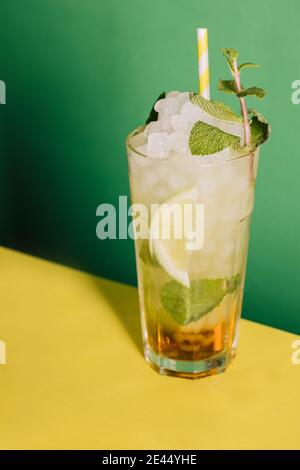 Ein Glas erfrischenden Alkohol Mojito Cocktail mit frischen Limetten und Eis garniert mit Minzblättern in der Nähe der grünen Wand platziert Stockfoto