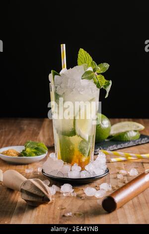 Ein Glas köstlichen erfrischenden Mojito Cocktail mit Limette und Eis Garniert mit frischer Minze auf dem Tisch in der Nähe von Holzpresse platziert Und Zutaten Stockfoto