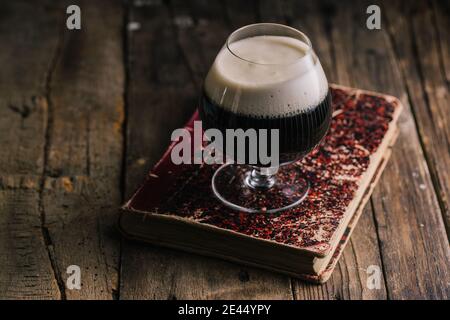 Hoher Winkel des Glases des dunklen Stout Bieres auf gelegt Altmodisches Buch auf einem schäbigen Holztisch Stockfoto