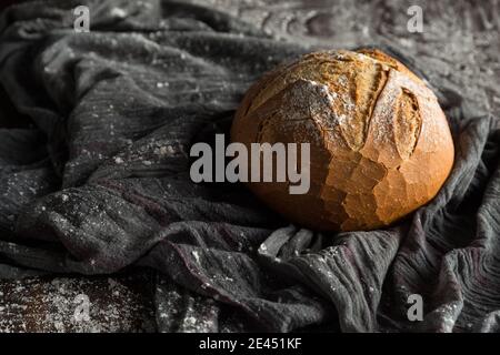 Von oben appetitlich frisch gebackenen runden Brot Laib Neben dem hölzernen Löffel auf dem grauen Tuch angeordnet, das mit dem Mehl bestreut ist Stockfoto