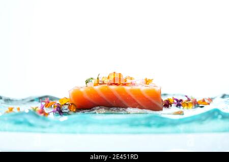 Stück appetitlichen Lachs Fisch mit bunten Blumen und verziert Kaviar und serviert auf hellblauem Tisch Stockfoto