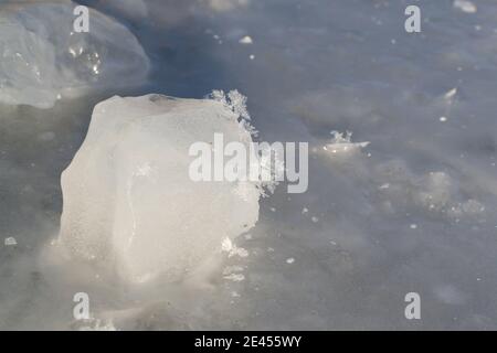 Mehrere Schneeflocken auf einem Stück Eis auf einem gefrorenen Fluss. Nahaufnahme. Horizontale Ausrichtung. Speicherplatz kopieren. Stockfoto