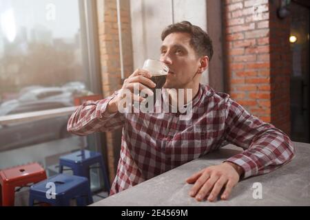 Junger Mann schlürft köstliches Craft-Bier, entspannt im Bierkneipe, Copy Space Stockfoto