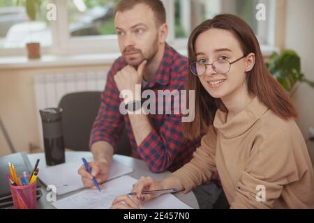 Fröhliche Teenager-Studentin lächelt zur Kamera, arbeitet an einem Projekt mit ihrem Lehrer, Copy Space. Hilfreicher Mentor Brainstorming mit seinen Teenagers Stockfoto