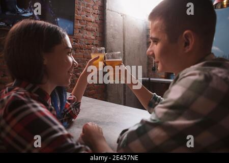 Junge liebende Paar toasten mit ihren Biergläsern, trinken in der Kneipe Stockfoto