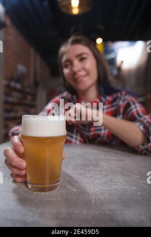 Selektiver Fokus auf Craft Bier im Glas im Hand einer jungen, liebenswerten Frau im Bierkneipe Stockfoto
