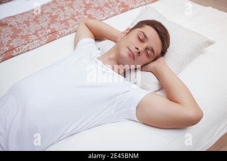 Junger Mann, der auf einem Bett schläft, sieht entspannt und ruhig aus Stockfoto