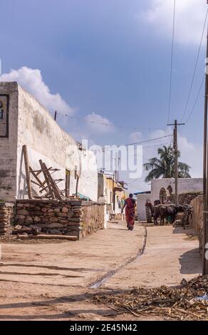 Lakundi, Karnataka, Indien - 6. November 2013: Typische Seitenstraße mit zentraler Rinne und weiß bemalten Häusern unter blauer Wolkenlandschaft. Müll und Schwarz Stockfoto