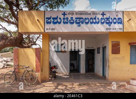 Lakundi, Karnataka, Indien - November 6, 2013: Primärversorgung Gesundheitszentrum Gebäude. Kombination von weißen und gelben Wänden mit blauen Buchstaben. Fahrrad und m Stockfoto