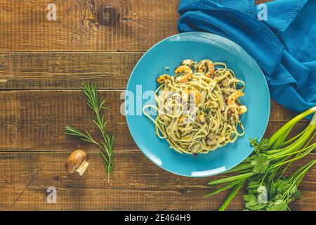 Pasta Linguine mit Pilzen, Garnelen und Meeresfrüchten Muscheln, Käse und Kräutern, in blauer Keramikplatte auf einer dunklen Holztischoberfläche. Stockfoto