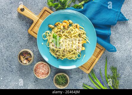 Pasta Linguine mit Pilzen, Garnelen und Meeresfrüchten Muscheln, Käse und Kräutern, in blauer Keramikplatte auf einer hellgrauen Oberfläche. Stockfoto