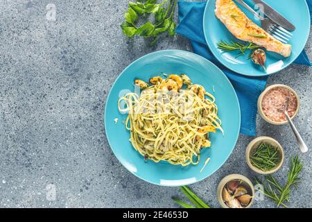 Pasta Linguine mit Pilzen, Garnelen und Meeresfrüchten Muscheln, Käse und Kräutern, in blauer Keramikplatte auf einer hellgrauen Oberfläche. Stockfoto