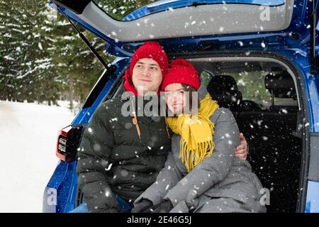 Romantisches junges Hipster-Paar umarmt, während im Kofferraum unter fallendem Schnee sitzt. Liebe, Valentinstag und Urlaubskonzept. Kuss und Umarmung. Valentinstag Stockfoto