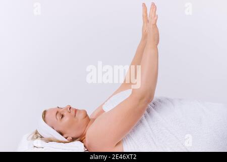 Eine zufriedene ältere Frau, die in einem Salon in ein weißes Handtuch gehüllt liegt und ihre hydratisierte und gesunde Haut nach den Spa-Behandlungen genießt. Stockfoto