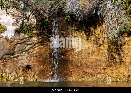 Ein kleiner Wasserbach stürzt sich an einem sonnigen Tag durch eine Sandsteinwand im Glen Canyon und mündet in den mächtigen Colorado River. Stockfoto