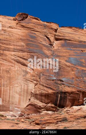 Die hoch aufragenden roten Sandsteinwände des Glen Canyon mit einem massiven Riss, der von oben nach unten läuft und von strahlendem Sonnenschein beleuchtet wird. Stockfoto