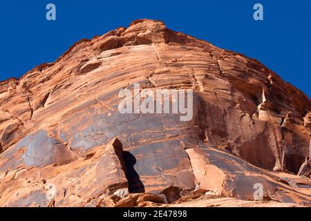 Die hoch aufragenden roten Sandsteinwände des Glen Canyon mit mehreren Rissen durch den alten Felsen, der von strahlendem Sonnenschein beleuchtet und von strahlendem blauen Himmel gekrönt ist. Stockfoto