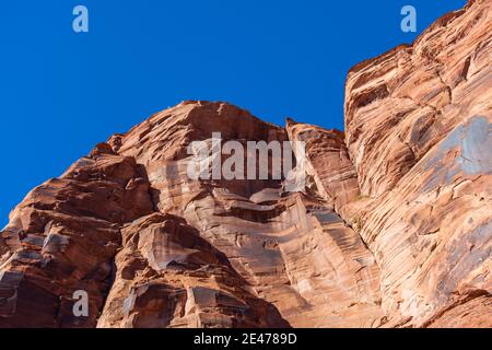 Die hoch aufragenden roten Sandsteinwände des Glen Canyon mit mehreren Rissen durch den alten Felsen, der von strahlendem Sonnenschein beleuchtet und von strahlendem blauen Himmel gekrönt ist. Stockfoto