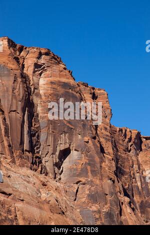 Die hoch aufragenden roten Sandsteinwände des Glen Canyon mit mehreren Rissen durch den alten Felsen, der von strahlendem Sonnenschein beleuchtet und von strahlendem blauen Himmel gekrönt ist. Stockfoto