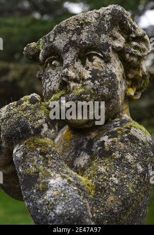 Eine Flechten und Moos bedeckte alte Steinstatue eines Cherubs, der auf dem Gelände des Hatley Castle in Colwood, British Columbia, Kanada, auf Vancouvert eine Flöte spielt Stockfoto