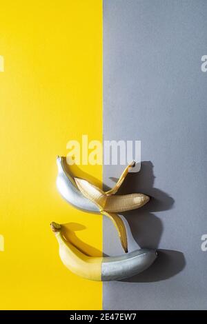Geschälte Bananen bemalt silberne Farbe auf einem gelb-grauen Hintergrund. Minimalistisches abstraktes Lebensmittelbild Stockfoto