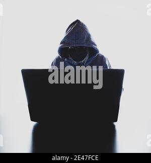 Hacker mit einer Gesichtsmaske und einer Kapuze davor Eines Laptops - Hack Angriff Konzept Stockfoto