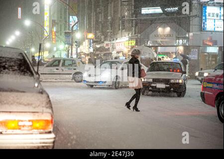 Eine Frau jayWalking auf einer belebten und verschneiten Straße während Schneesturm in einer japanischen Stadt. Stockfoto