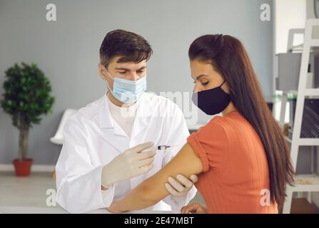 Mittleren Alters zuversichtlich Mann Arzt in weißer Uniform und medizinische Maske macht Injektion dor Frau Stockfoto
