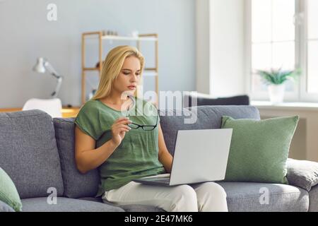 Fokussierte Freiberuflerin Frau, die auf einem Laptop sitzt auf dem Sofa im Wohnzimmer ihres Hauses. Stockfoto