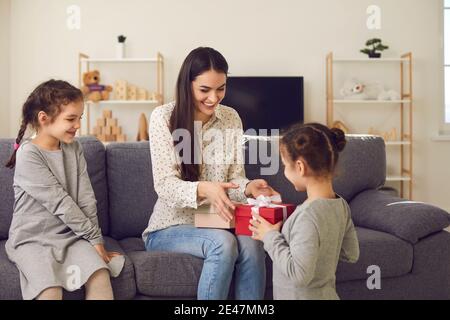 Glückliche junge Mutter bekommt Weihnachtsgeschenke in festlichen Schachteln von Ihre Töchter Stockfoto