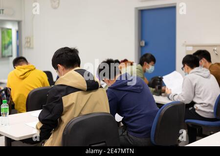 Schüler mit Gesichtsmaske lesen und machen Kursarbeit im Klassenzimmer In der Universität in Hong Kong während Covid-19 Stockfoto