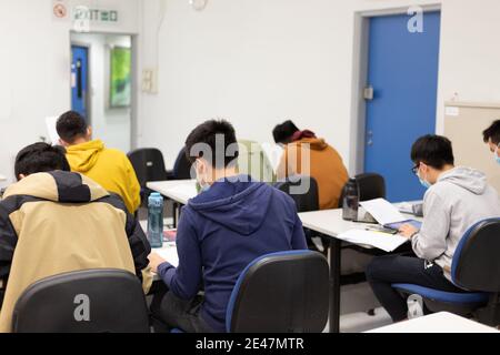 Schüler mit Gesichtsmaske lesen und machen Kursarbeit im Klassenzimmer In der Universität in Hong Kong während Covid-19 Stockfoto