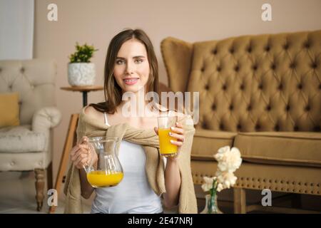 Lächelndes Mädchen mit Klammern hält Glas und Krug mit Saft in den Händen Stockfoto